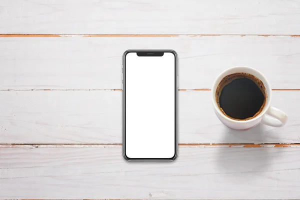 Mobiele telefoon met x scherm op witte houten tafel. Kopje koffie naast. Bovenaanzicht. — Stockfoto