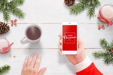 Noel Baba mutlu Noeller cep telefonu ile mesaj gönderin. Sıcak çay ve Noel dekorasyonu yanında.