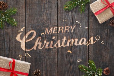 Metin el tebrik Noel Noel süslemeleri ile koyu ahşap yüzey üzerine oyulmuştur. Hediyeler, çam dalları ve pinecones yanında.