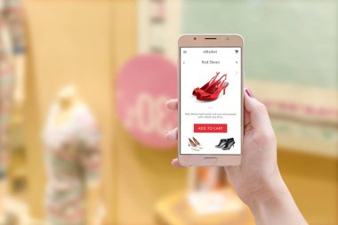 Akıllı tutan kadın ile online mağaza app ekranda ön görünüm telefon. Arka planda indirimlerle penceredir.