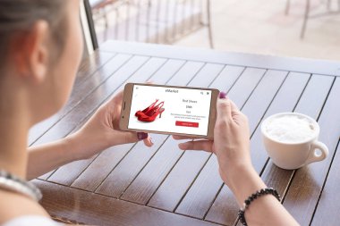Kız alışveriş online ve arama ayakkabılar için. Cep telefonu yatay pozisyonda. Kahve.