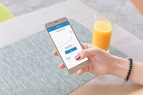 Kripto para birimi grafik akıllı telefon uygulama kadın holding telefon üzerinde. Suyu ve tablo arka planda.