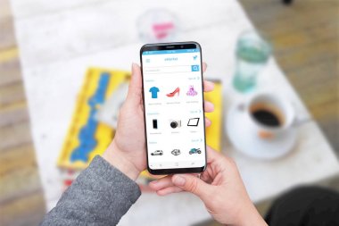Online web sitesi ya da app modern akıllı telefonun ekranında yuvarlak kenarlı saklayın. Kahve dükkanında arka plan.