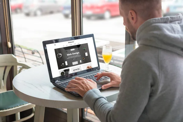 Visitor open a responsible website of the design company on his laptop. Coffee shop in background.