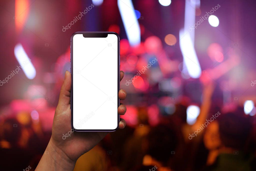 Modern mobile phone in woman hand with isolated screen for mockup. Live music concert and crowd in background.