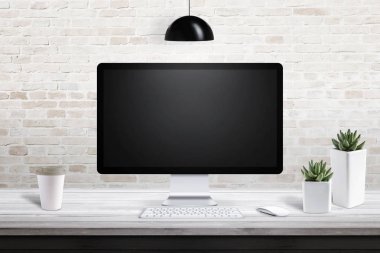 Bilgisayar göster bitkiler nad plastik bardak kahve ile modern ofis masasında. Tuğla duvar arka planda.