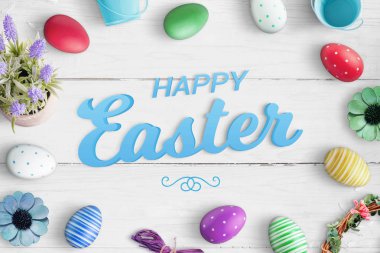 Mutlu Paskalya metin renkli yumurta ve çiçek süslemeleri ile çevrili beyaz ahşap masa mavi.
