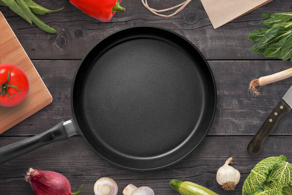 Empty pan on a kitchen table surrounded by vegetarian cuisine ingredients.