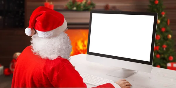 圣诞老人在壁炉和圣诞树旁的电脑上工作 圣诞贺卡概念与孤立的计算机显示的问候文字 — 图库照片