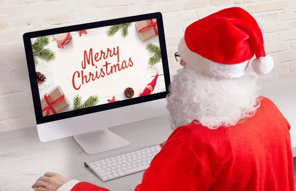 サンタはコンピュータ上のクリスマスカードを設計します コンピュータディスプレイ上のメリークリスマスグリーティングカードの概念 — ストック写真