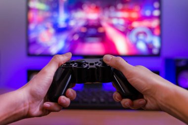 Joypad 'in elinde. Oyun konsepti. Arka planda yarış oyunu ve rgb ışığı ile bilgisayar görüntüsü.