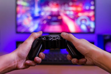 Joypad in hands. Gaming concept. Computer display with racing game and rgb light in background. clipart