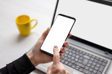 Kadının ellerindeki izole ekranlı telefon. Laptop ve kahve arka planda. Uygulama veya web sitesi sunumu için çalışma kavramı