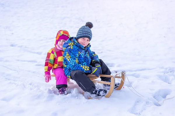 女孩和男孩在雪橇上 身穿冬衣 头戴帽子 戴手套的兄妹 — 图库照片