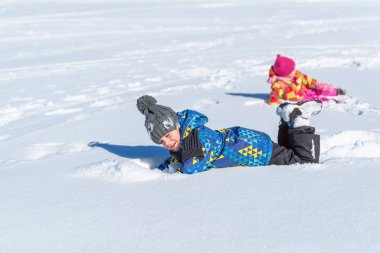 Oğlan ve kız karda yuvarlanıyorlar. Kış tatili kavramı ve çocukların karda mutluluğu ve neşesi