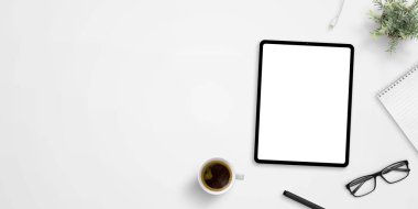 Tablet maketi ve negatif alanı olan ofis masası. Bir fincan kahve, bitki, bardak, kalem ve ped yanında. Kahraman, başlık resmi veya afiş bileşimi
