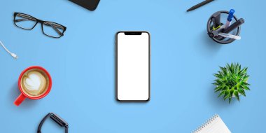 Ofis malzemeleri ile çevrili mavi ofis masasında telefon modeli. Model, web sitesi veya uygulama sunumu için izole ekran. Top vie, flat lay