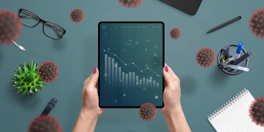 Coronavirus 'un küresel ekonomi ve kadın elinde tablet ekrandaki pazarlar üzerindeki etkilerinin grafikleri. Üst görünüm, düz konum