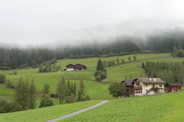 ST. MAGDALENA, ITALY - SEPTEMBER 14, 2015: Traditional houses in a cloudy mornig surrounded by green pasture next to the little town of St. Magdalena in Val di Funes, no people around — Stock Photo, Image