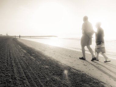 Jesolo, İtalya - 27 Ağustos 2017: iki yaşlı insanlar yan yana uzun yürüyüş bir İtalyan sahil plaj sabahın erken saatlerinde