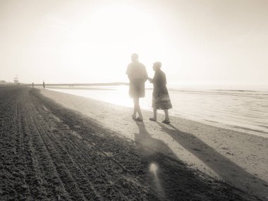 Jesolo, İtalya - 27 Ağustos 2017: iki yaşlı insanlar yan yana uzun yürüyüş bir İtalyan sahil plaj sabahın erken saatlerinde