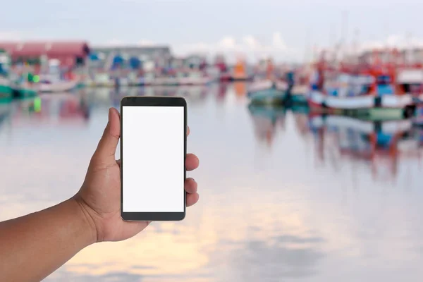 Un teléfono de mano sobre muchos pequeños barcos de pesca en el puerto . — Foto de Stock