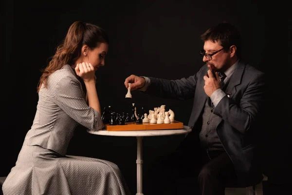 En man med en tjej spelar schack och röker pipa på en mörk bakgr — Stockfoto