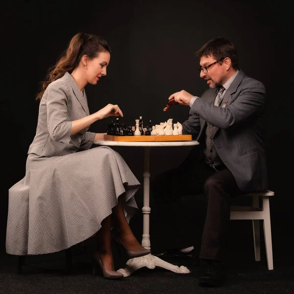 En man med en tjej spelar schack och röker pipa på en mörk bakgr — Stockfoto