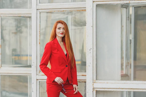 Beautiful girl with red hair dressed in a red business suit. Bus — Stock Photo, Image
