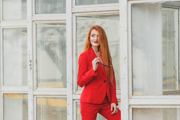 Beautiful girl with red hair dressed in a red business suit. Bus — Stock Photo, Image