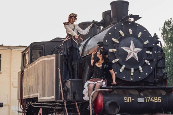 Two beautiful girl in steampunk clothes on the background of the train close-up