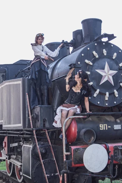 Two beautiful girl in steampunk clothes on the background of the train close-up