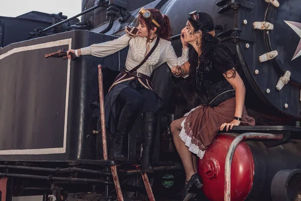 Two beautiful girl in steampunk clothes on the background of the train close-up