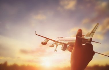 close up photo of man's hand holding toy airplane and sunset background clipart