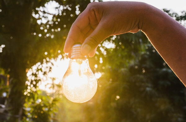 hand holding a light bulb with sunset power concept