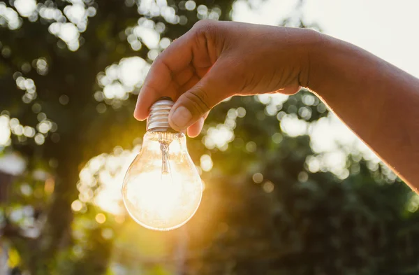 Hand hält eine Glühbirne mit Sonnenuntergangskonzept — Stockfoto