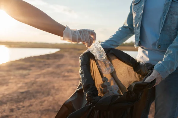 Freiwillige halten Müllplastikflasche in schwarzen Sack — Stockfoto