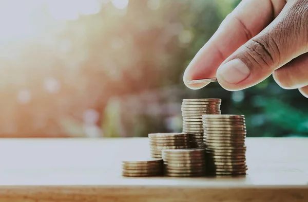 Εξοικονόμηση χρημάτων χέρι βάζοντας κέρματα σε στοίβα στο τραπέζι με ήλιο. — Φωτογραφία Αρχείου