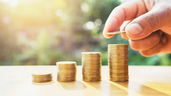 Εξοικονόμηση χρημάτων χέρι βάζοντας κέρματα σε στοίβα στο τραπέζι με ήλιο. — Φωτογραφία Αρχείου