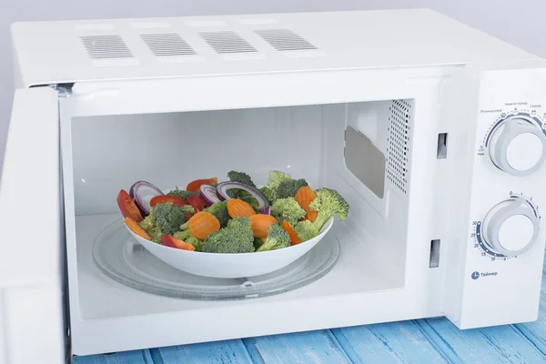 Un nuevo horno de microondas blanco, sobre una superficie de madera azul para calentar —  Fotos de Stock