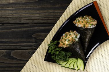 Siyah arka planda siyah tabakta somon temaki suşisi.