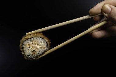 Çırpılmış suşi, sıcak rulo. Yemek çubuğuyla suşi toplayan bir kadın. Siyah arkaplan.