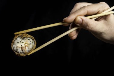 Çırpılmış suşi, sıcak rulo. Yemek çubuğuyla suşi toplayan bir kadın. Siyah arkaplan.