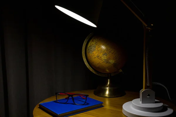 Detail of center table with lamp, book, glasses and globe.