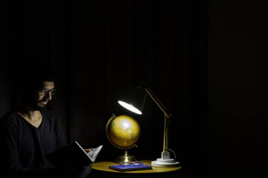 Koltukta oturan adam bir kitap okumaya konsantre oldu. Aydınlatıcı lamba ile koyu arkaplan.