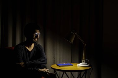 Koltukta oturan adam bir kitap okumaya konsantre oldu. Aydınlatıcı lamba ile koyu arkaplan.