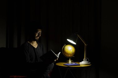 Koltukta oturan adam bir kitap okumaya konsantre oldu. Aydınlatıcı lamba ile koyu arkaplan.