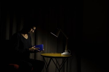 Koltukta oturan adam bir kitap okumaya konsantre oldu. Aydınlatıcı lamba ile koyu arkaplan.