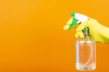 Sarı koruyucu eldivenli bir adam turuncu arka planı sterilize etmek için sprey şişesi tutuyor. Yüzey konsepti siliniyor.