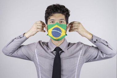 Man putting on mask with Brazil country flag (covid-19, coronavirus, SARS-CoV-2). clipart